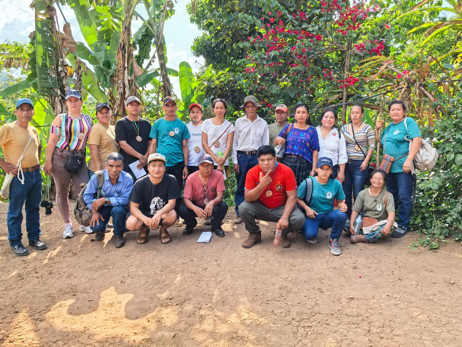 Grupo de meliponicultoras y meliponicultores reunidos en el campo, entre bananos y bugambilias